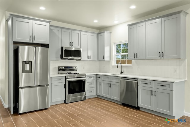 kitchen with stainless steel appliances, sink, tasteful backsplash, and light hardwood / wood-style flooring