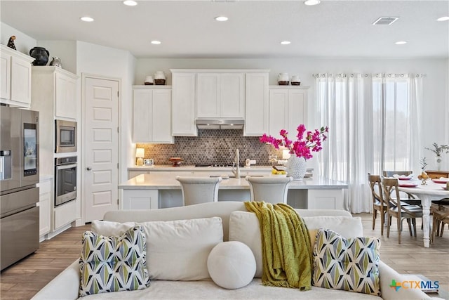 kitchen with tasteful backsplash, stainless steel appliances, a center island with sink, hardwood / wood-style floors, and white cabinetry