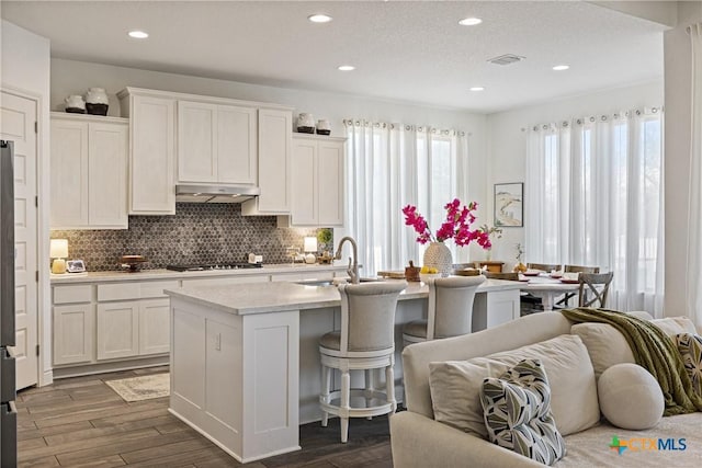 kitchen with white cabinetry, sink, dark wood-type flooring, stainless steel gas stovetop, and a kitchen island with sink