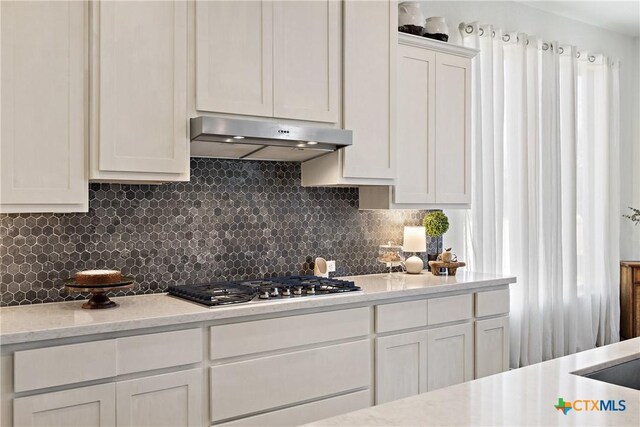 kitchen featuring decorative backsplash, white cabinetry, stainless steel gas cooktop, and range hood