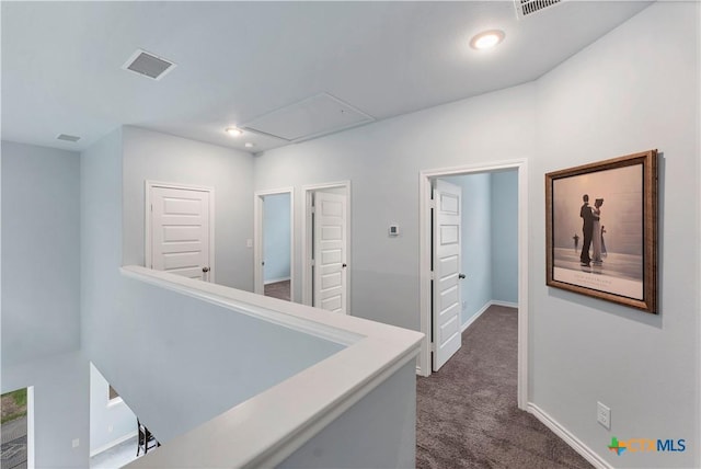 corridor with attic access, visible vents, dark colored carpet, and baseboards