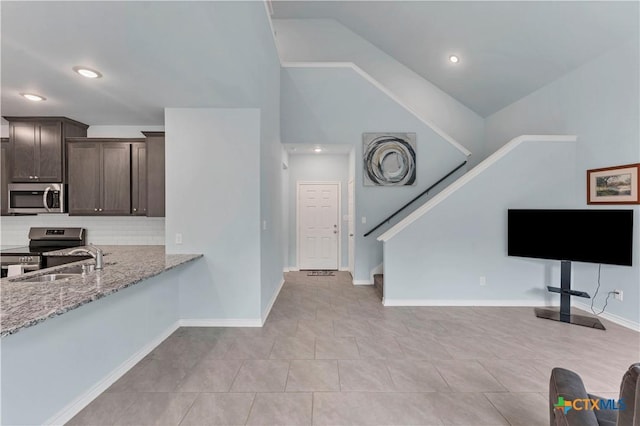 kitchen featuring light stone counters, dark brown cabinetry, baseboards, appliances with stainless steel finishes, and backsplash