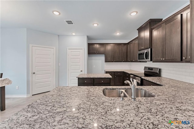 kitchen featuring dark brown cabinetry, visible vents, light stone counters, stainless steel appliances, and a sink