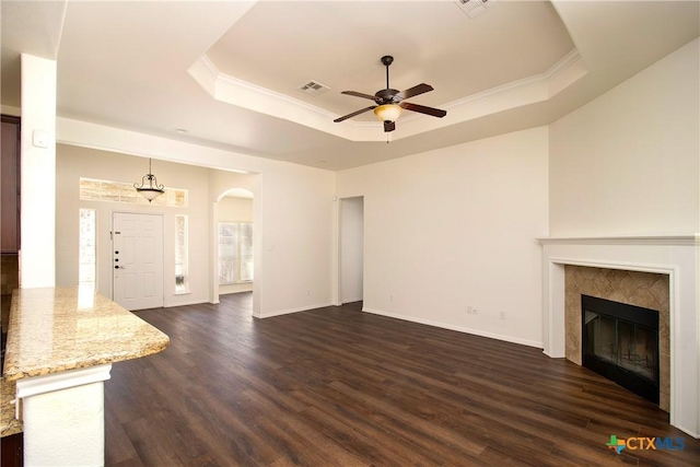 unfurnished living room featuring arched walkways, dark wood-style flooring, crown molding, a raised ceiling, and a tile fireplace