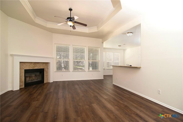 unfurnished living room featuring baseboards, a raised ceiling, a tiled fireplace, dark wood-style floors, and ornamental molding