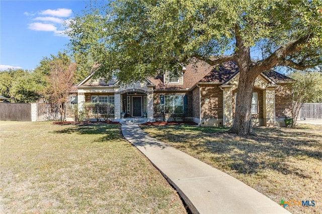 view of front of property featuring stone siding, a front lawn, fence, and brick siding