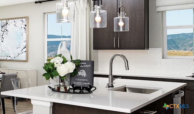 kitchen featuring dark brown cabinetry, sink, decorative light fixtures, an island with sink, and decorative backsplash