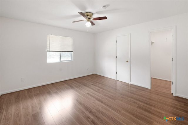 unfurnished bedroom featuring hardwood / wood-style floors, ceiling fan, and a walk in closet