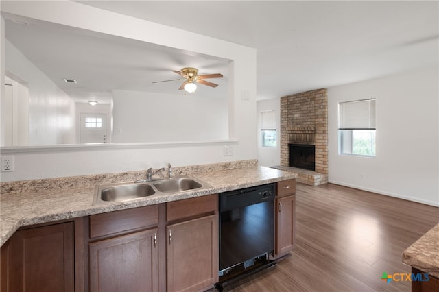 kitchen with a brick fireplace, dark wood-type flooring, black dishwasher, sink, and ceiling fan