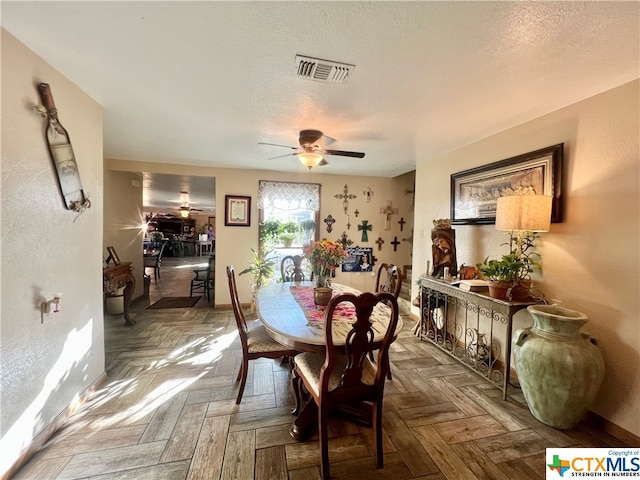 dining space with ceiling fan, dark parquet flooring, and a textured ceiling