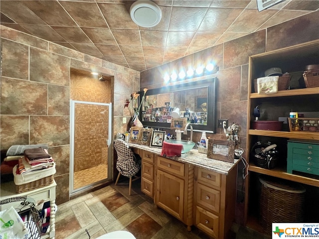 bathroom featuring walk in shower, vanity, and tile walls