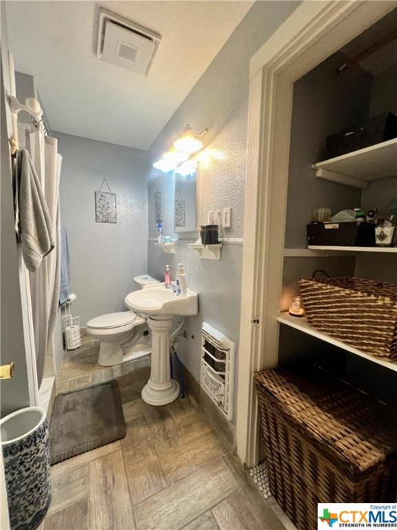 bathroom with toilet, sink, heating unit, and hardwood / wood-style floors