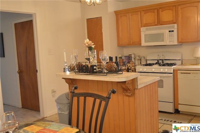 kitchen with white appliances, light tile patterned floors, an inviting chandelier, a breakfast bar area, and kitchen peninsula