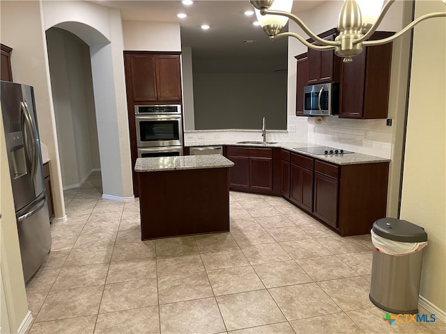 kitchen with stainless steel appliances, sink, tasteful backsplash, light stone countertops, and a center island