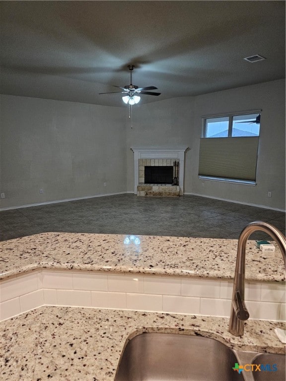 interior space featuring sink, light stone counters, ceiling fan, and a fireplace