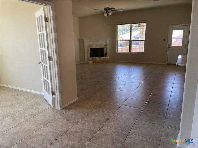 unfurnished living room with a tiled fireplace, light tile patterned floors, and ceiling fan