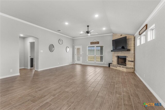 unfurnished living room with arched walkways, a wealth of natural light, a stone fireplace, and wood finished floors