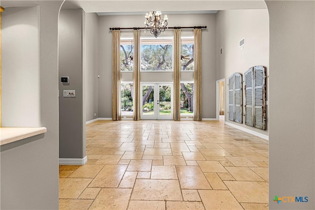 313 Treasure Oaks Rd, Inez, TX 77968 - unfurnished dining area featuring stone tile floors, baseboards, arched walkways, a chandelier, and a towering ceiling