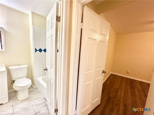 bathroom featuring tiled shower / bath, vaulted ceiling, a textured ceiling, and toilet