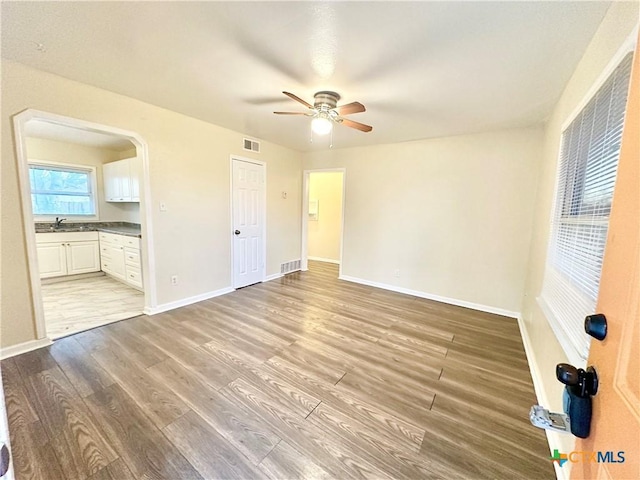 unfurnished bedroom featuring connected bathroom, sink, light hardwood / wood-style flooring, and ceiling fan