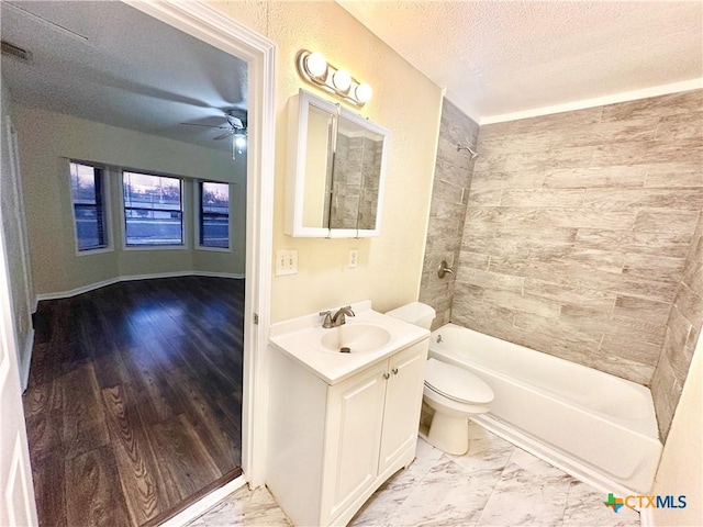 full bathroom with ceiling fan, vanity, a textured ceiling, toilet, and tiled shower / bath