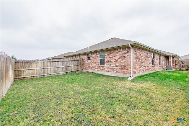 rear view of house with a fenced backyard, central AC, a lawn, and brick siding