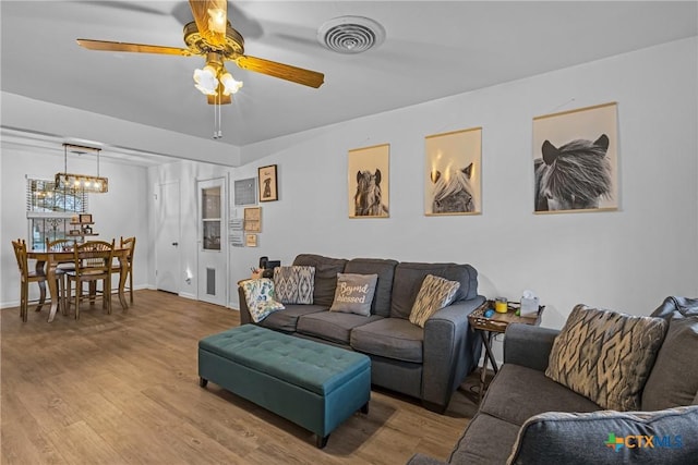 living room featuring ceiling fan with notable chandelier, visible vents, baseboards, and wood finished floors