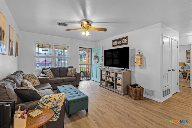 living area with light wood-style floors, ceiling fan, visible vents, and baseboards