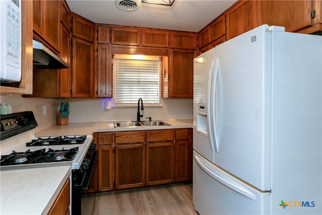 kitchen with range hood, light wood-type flooring, white appliances, and sink