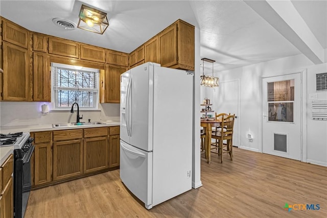 kitchen featuring light wood-style flooring, brown cabinets, black range with gas stovetop, white fridge with ice dispenser, and a sink