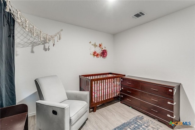 bedroom featuring a crib, visible vents, and wood finished floors