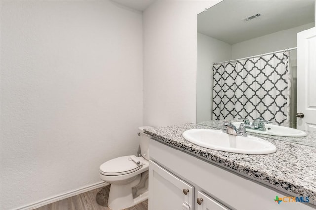 full bath with baseboards, visible vents, toilet, wood finished floors, and vanity