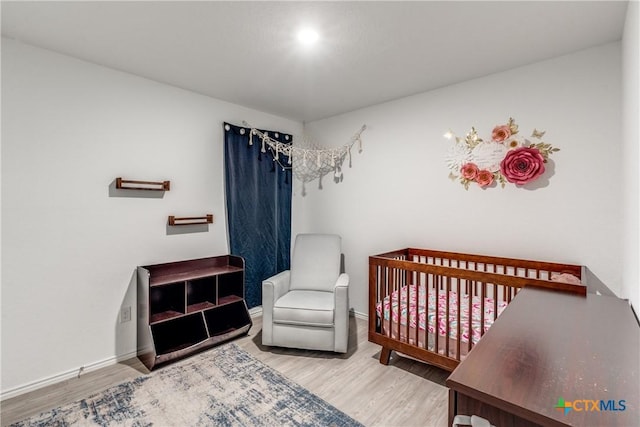 bedroom with a crib, baseboards, and wood finished floors