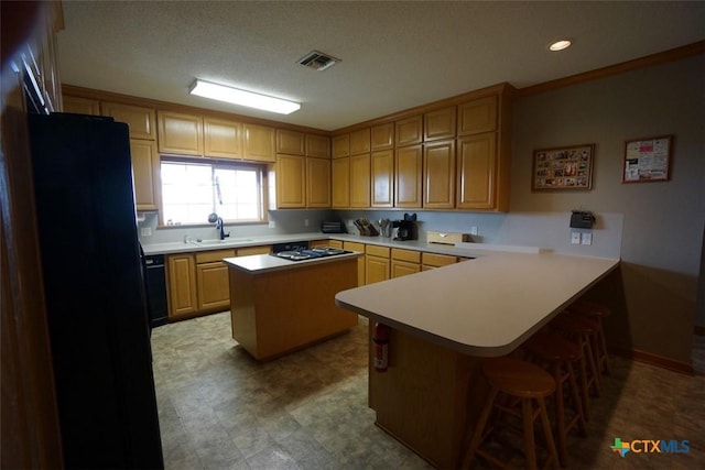 kitchen featuring sink, a textured ceiling, a kitchen breakfast bar, a kitchen island, and black appliances