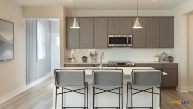 544 Bauer Loop, Liberty Hill, TX 78642 - kitchen with appliances with stainless steel finishes, wood finished floors, a kitchen breakfast bar, hanging light fixtures, and light countertops