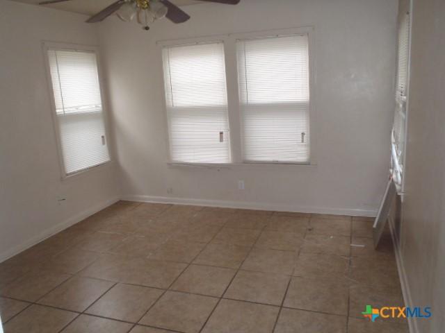 empty room with baseboards, a ceiling fan, and light tile patterned flooring