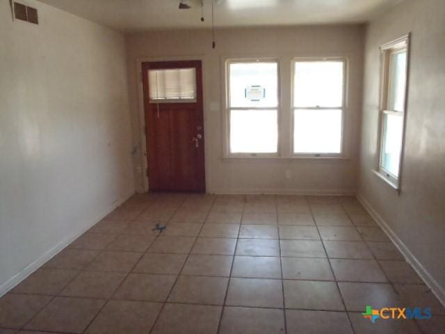 interior space with light tile patterned flooring, visible vents, a ceiling fan, and baseboards