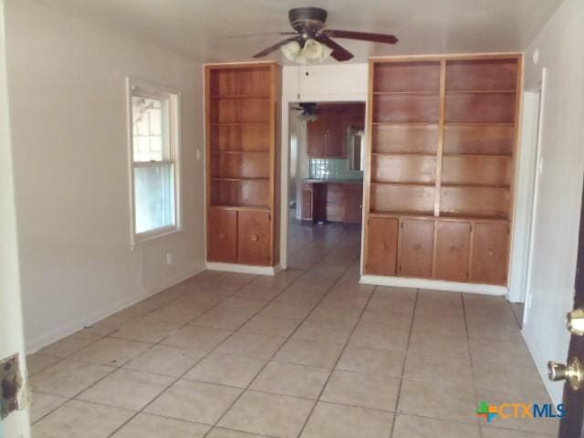 unfurnished room featuring light tile patterned flooring, ceiling fan, built in shelves, and baseboards
