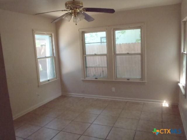 empty room featuring light tile patterned floors, a ceiling fan, and baseboards