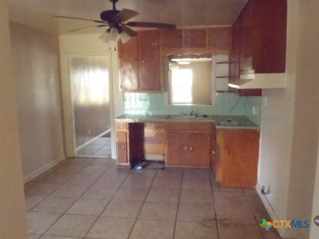 kitchen with light tile patterned floors, ceiling fan, light countertops, and brown cabinetry