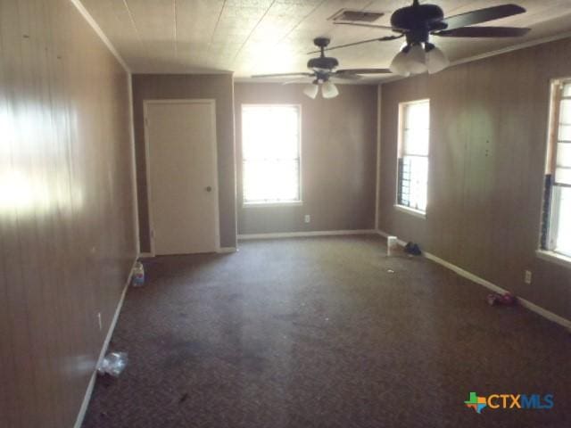 unfurnished room with wooden walls, a ceiling fan, visible vents, and baseboards
