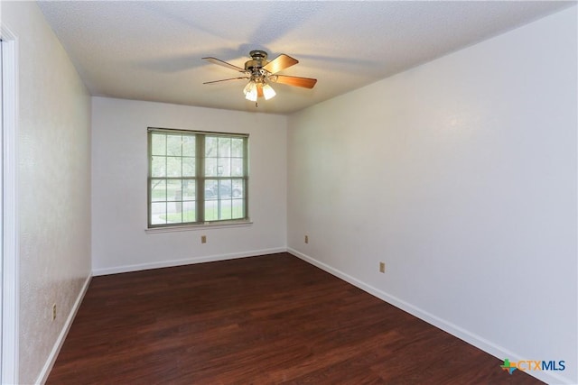 empty room with dark wood-style floors, a ceiling fan, and baseboards