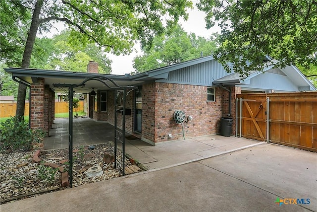 view of side of property featuring brick siding, a chimney, a patio area, a gate, and fence