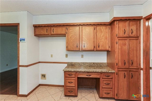 kitchen featuring brown cabinetry, light tile patterned floors, a textured ceiling, and baseboards