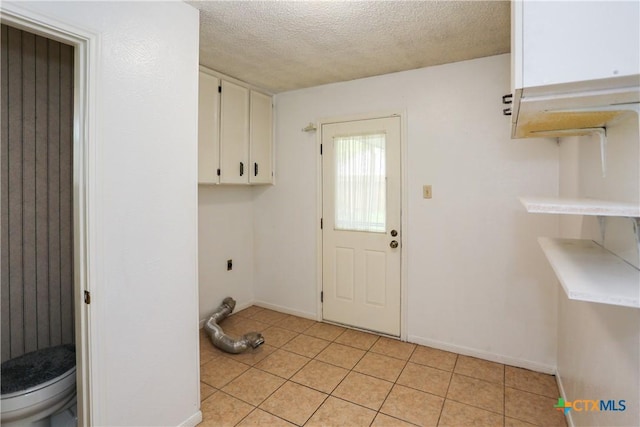 washroom featuring cabinet space, a textured ceiling, hookup for an electric dryer, light tile patterned flooring, and baseboards