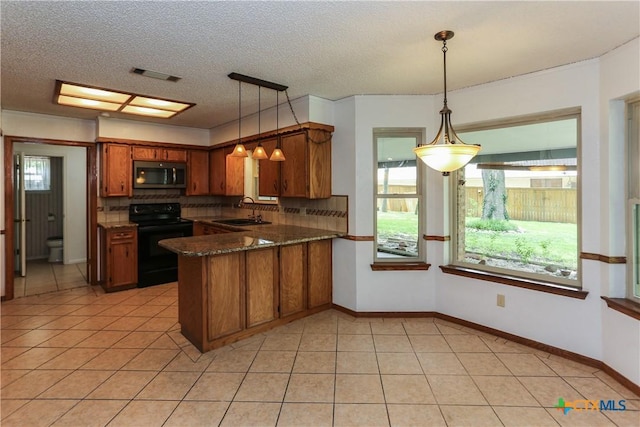 kitchen with black range with electric cooktop, stainless steel microwave, a sink, brown cabinetry, and a peninsula