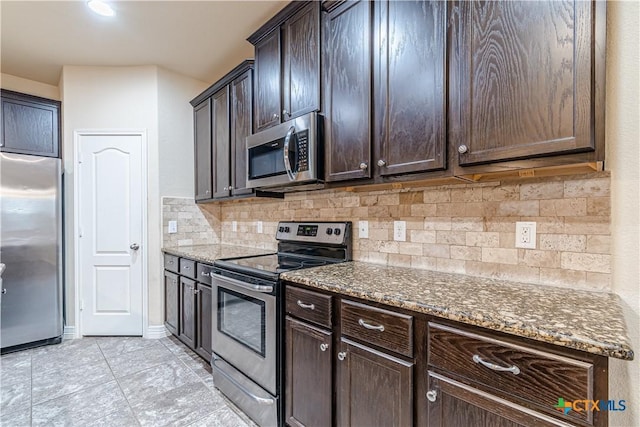 kitchen featuring dark brown cabinetry, stainless steel appliances, decorative backsplash, and dark stone countertops