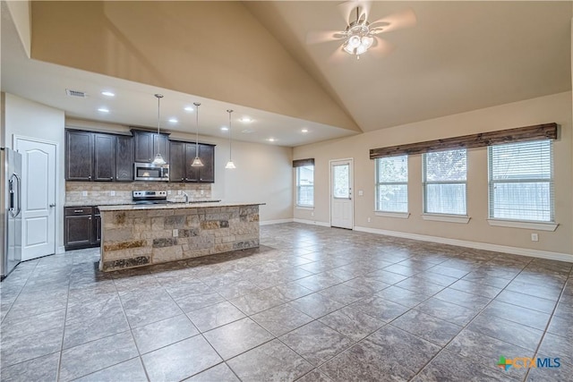 kitchen featuring decorative light fixtures, backsplash, a kitchen island with sink, dark brown cabinetry, and stainless steel appliances