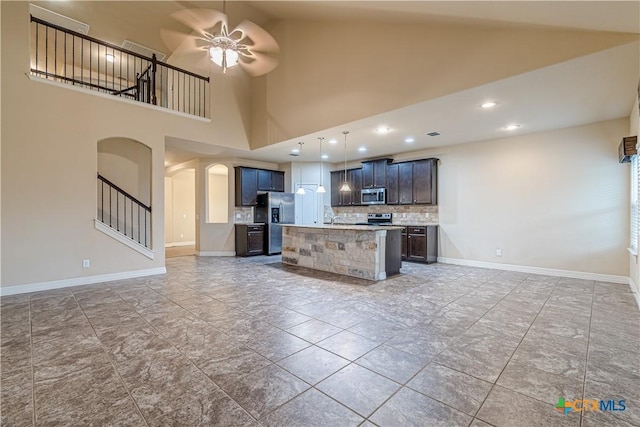 kitchen featuring ceiling fan, stainless steel appliances, decorative backsplash, a center island with sink, and decorative light fixtures