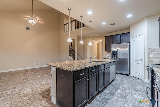 kitchen with sink, stainless steel appliances, light stone countertops, a center island with sink, and decorative light fixtures